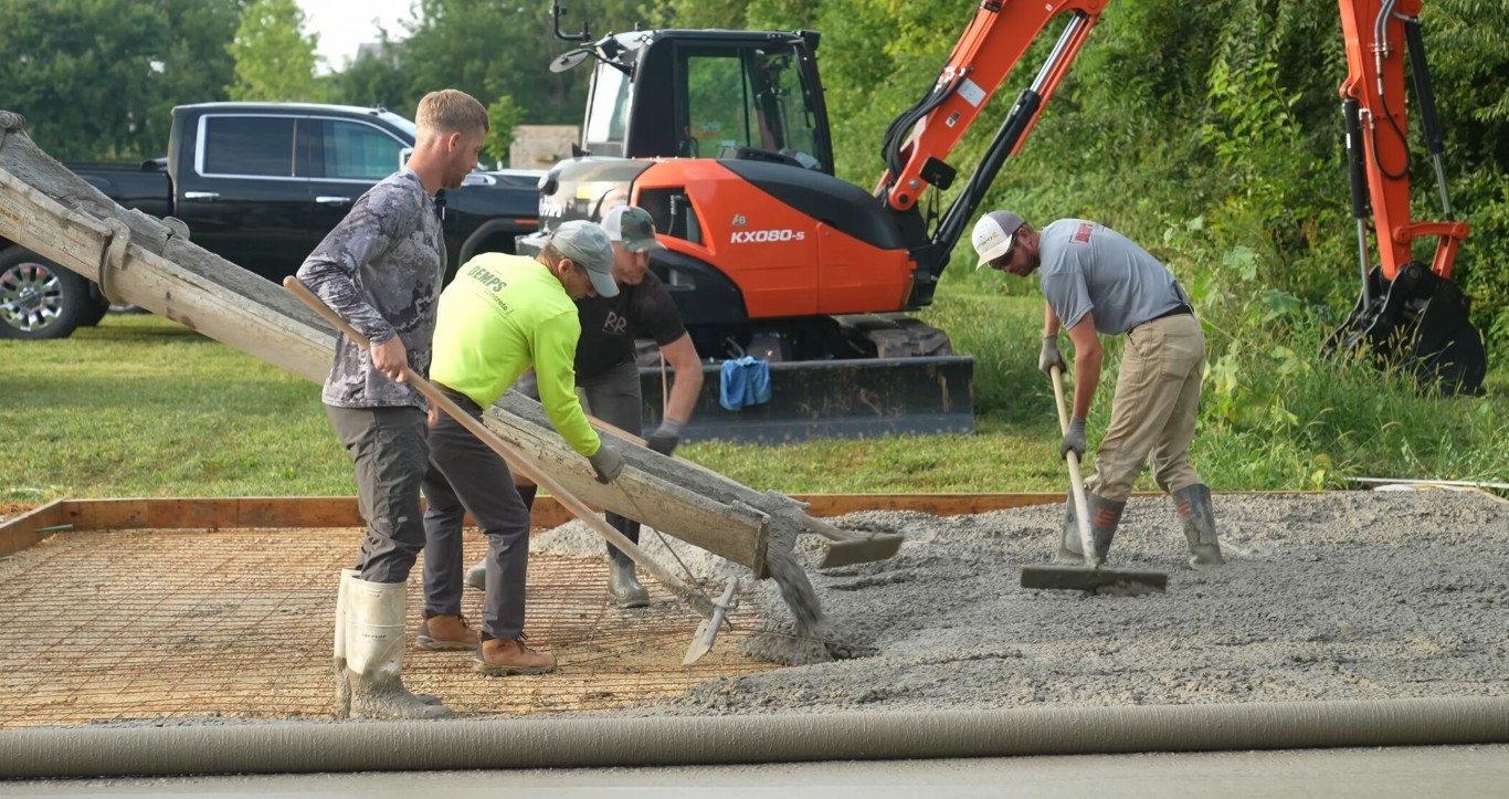 Commercial concrete contractor crew pouring a large reinforced concrete slab with excavator on site